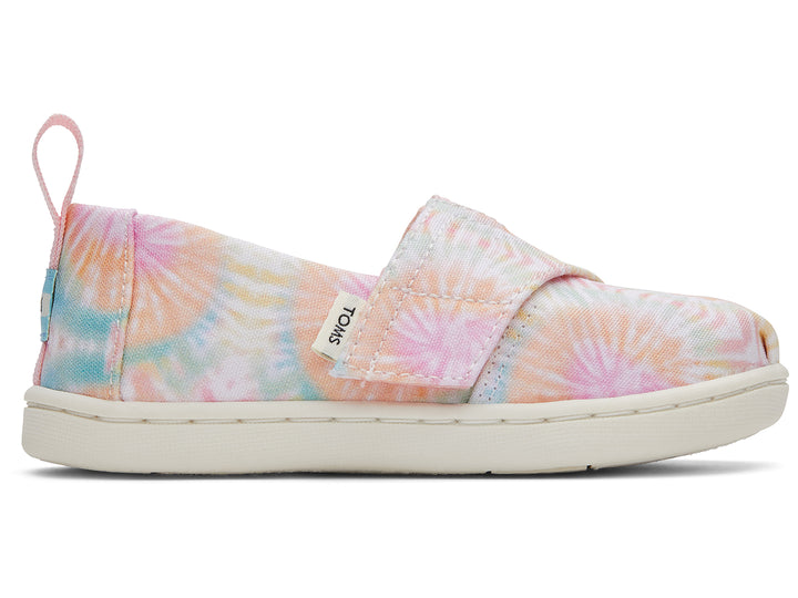 Par de zapatos TOMS estilo slip-on con estampado tie dye en tonos rosa, amarillo y azul con suela blanca.