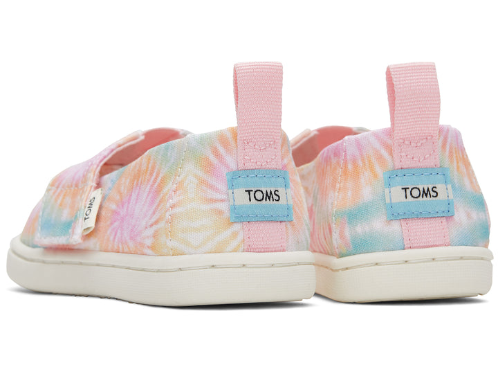 Par de zapatos TOMS estilo slip-on con estampado tie dye en tonos rosa, amarillo y azul con suela blanca.