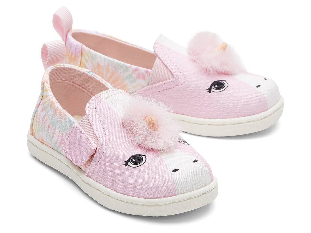 Zapatos infantiles TOMS color rosa con diseño de unicornio, pompones y detalles en tie-dye.