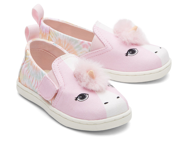 Zapatos infantiles TOMS color rosa con diseño de unicornio, pompones y detalles en tie-dye.