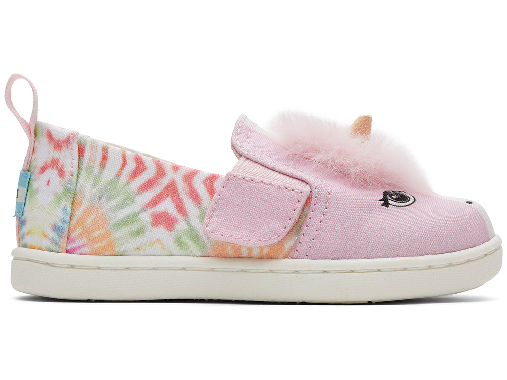 Zapatos infantiles TOMS color rosa con diseño de unicornio, pompones y detalles en tie-dye.