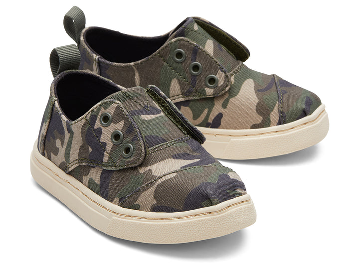 Par de zapatos infantiles TOMS con estampado de camuflaje en tonos verdes y beige, suela clara y diseño casual.