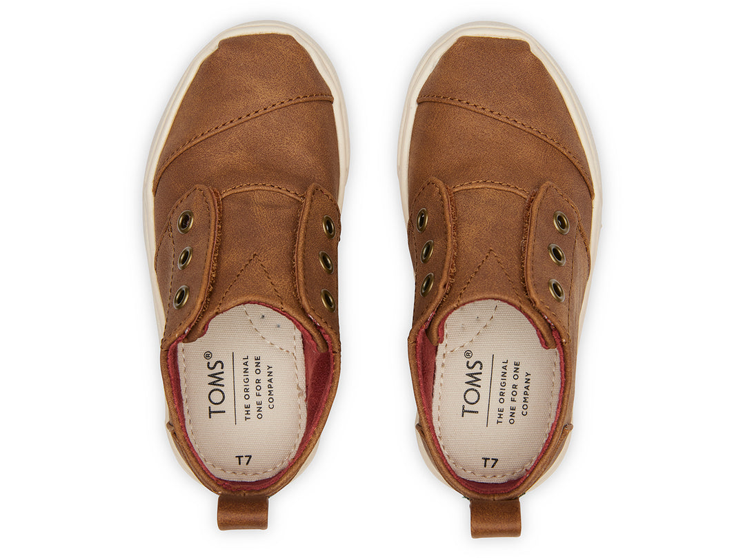 Zapato casual infantil TOMS color café toffee con suela blanca y diseño sin cordones.