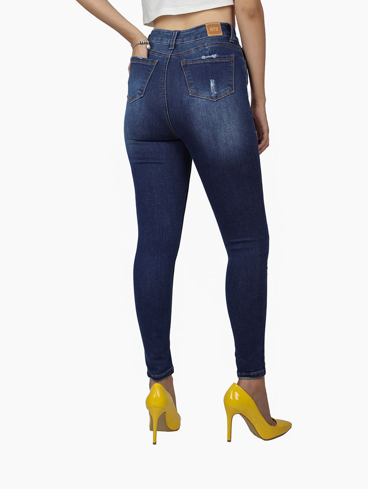 Mujer vistiendo pantalón de mezclilla azul oscuro ajustado con detalles desgastados.