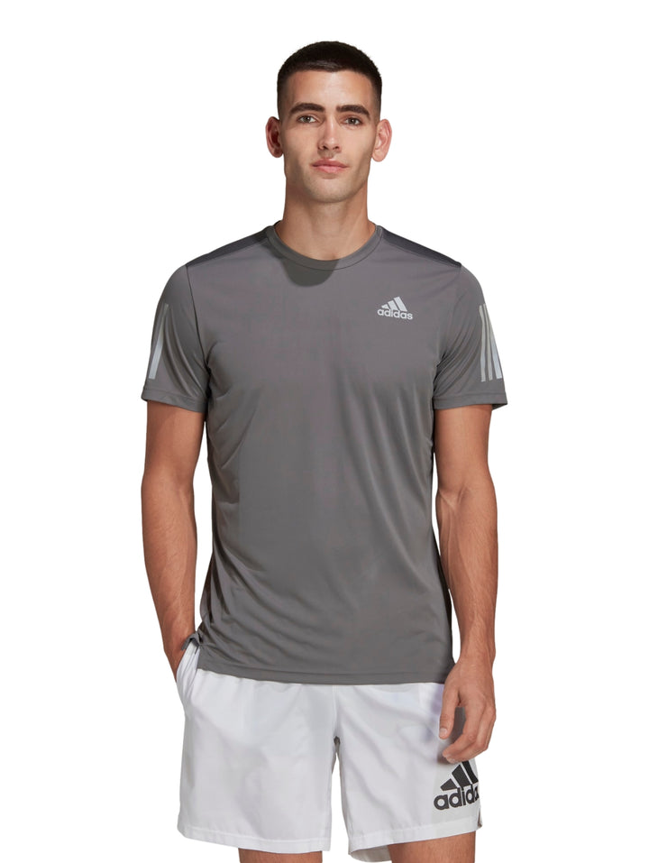 Hombre vistiendo playera deportiva Adidas color gris con detalles reflectantes y shorts blancos.