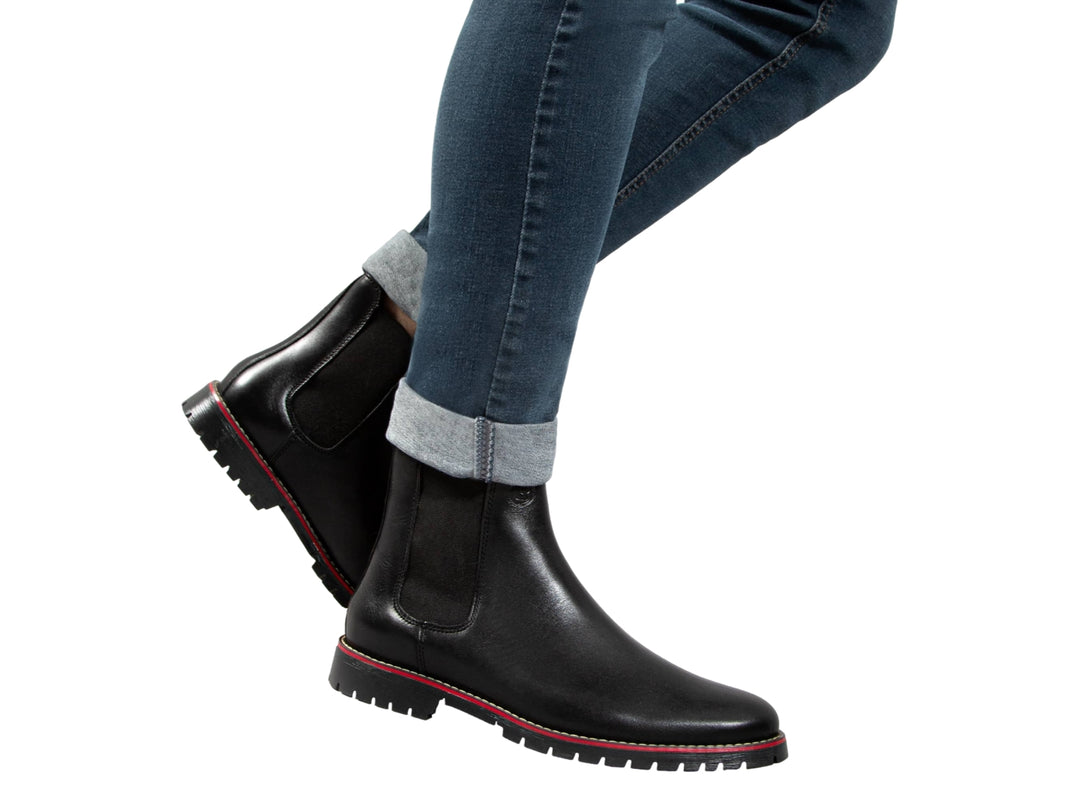 Botín negro de piel para hombre con detalle rojo en la suela y panel elástico lateral.