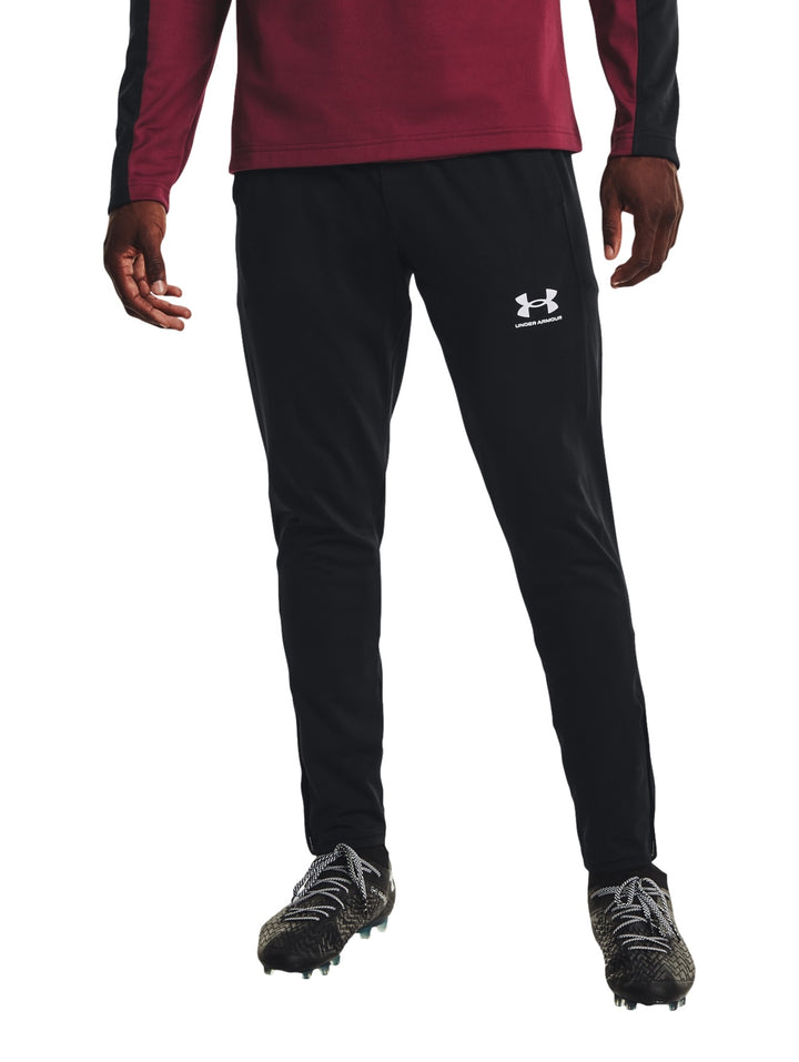 Hombre vistiendo pantalones deportivos Under Armour color negro con logo blanco en la pierna izquierda.