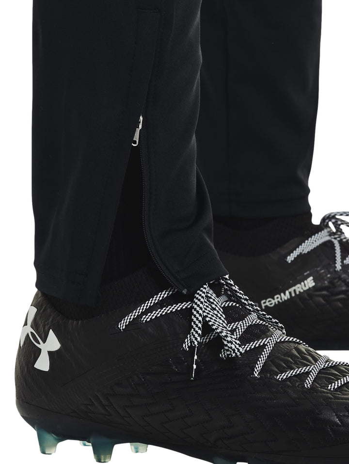 Hombre vistiendo pantalones deportivos Under Armour color negro con logo blanco en la pierna izquierda.