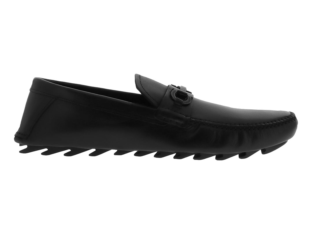 Zapato mocasín negro de cuero con suela track gruesa y detalle metálico en el empeine.