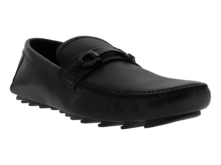 Zapato mocasín negro de cuero con suela track gruesa y detalle metálico en el empeine.