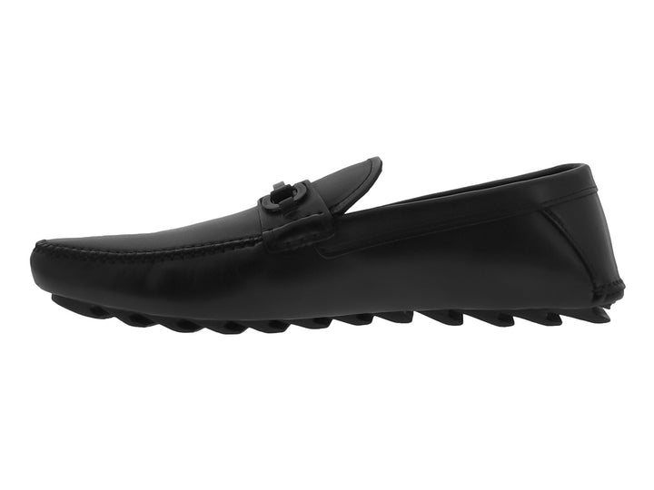 Zapato mocasín negro de cuero con suela track gruesa y detalle metálico en el empeine.