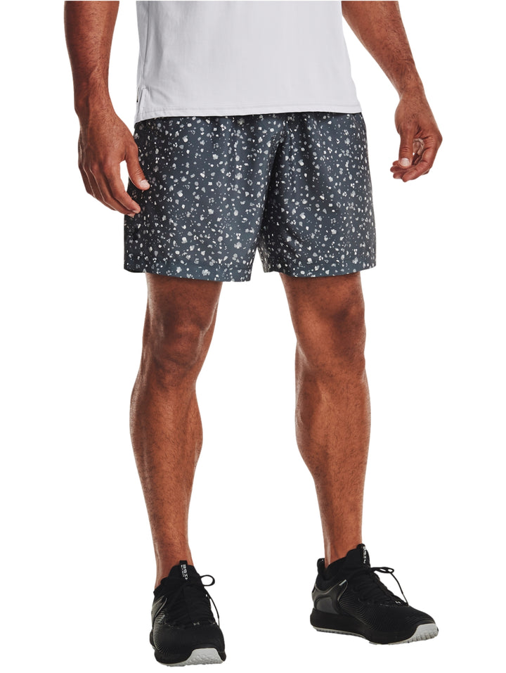 Hombre vistiendo shorts deportivos Under Armour color gris oscuro con estampado de puntos blancos.