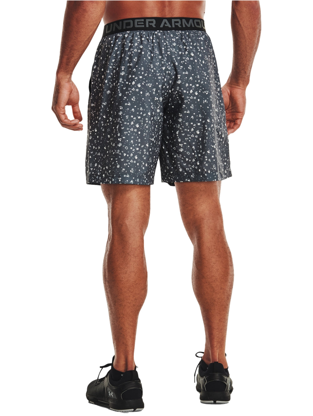 Hombre vistiendo shorts deportivos Under Armour color gris oscuro con estampado de puntos blancos.