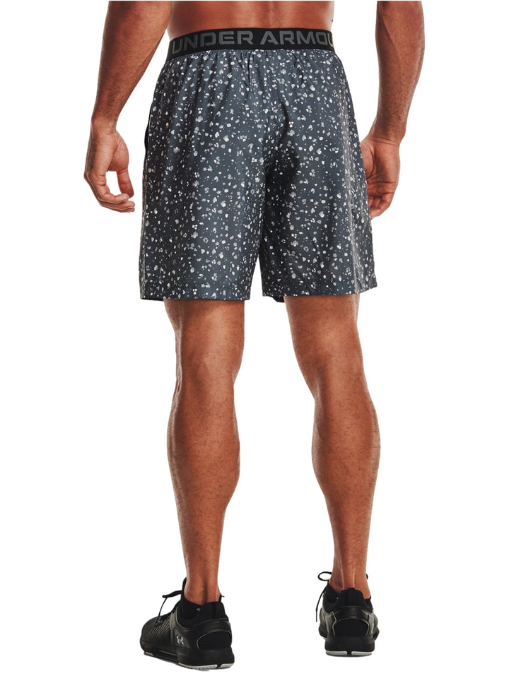 Hombre vistiendo shorts deportivos Under Armour color gris oscuro con estampado de puntos blancos.