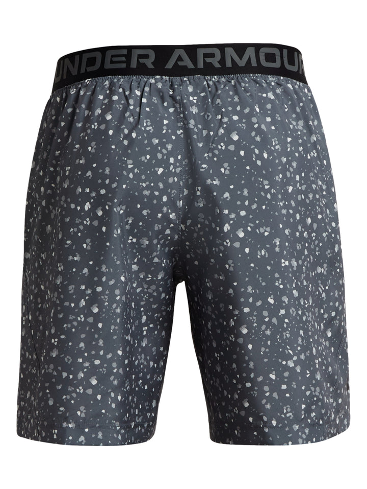 Hombre vistiendo shorts deportivos Under Armour color gris oscuro con estampado de puntos blancos.