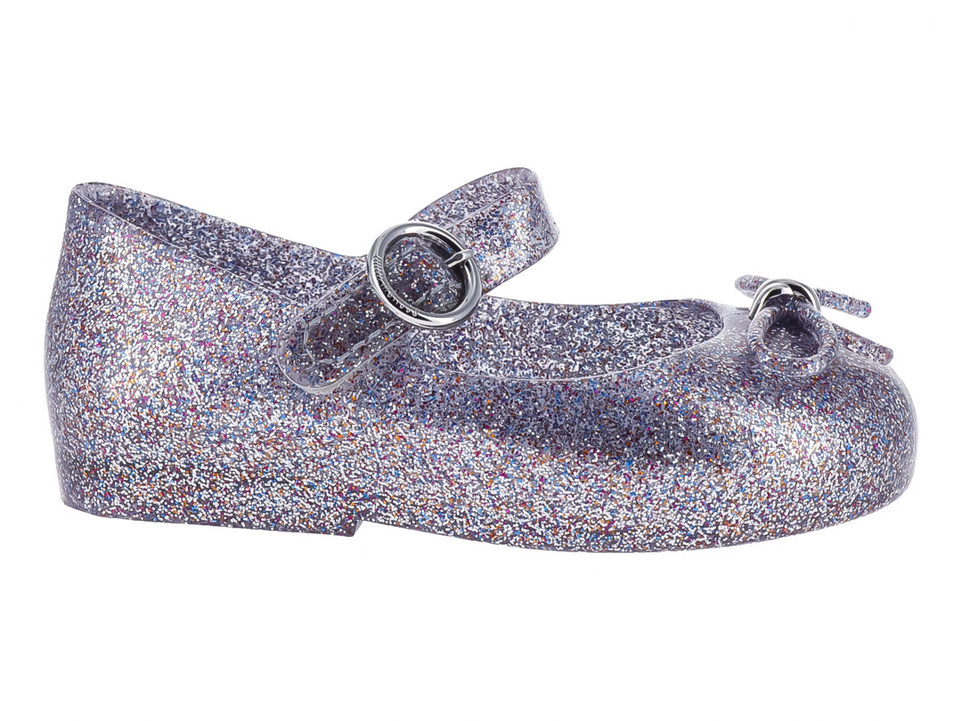 Zapato infantil color plata con acabado de glitter brillante y cierre de hebilla.