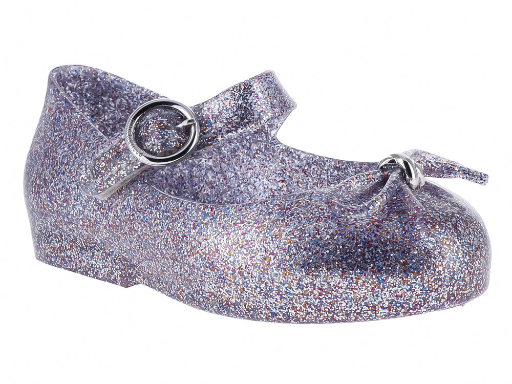 Zapato infantil color plata con acabado de glitter brillante y cierre de hebilla.