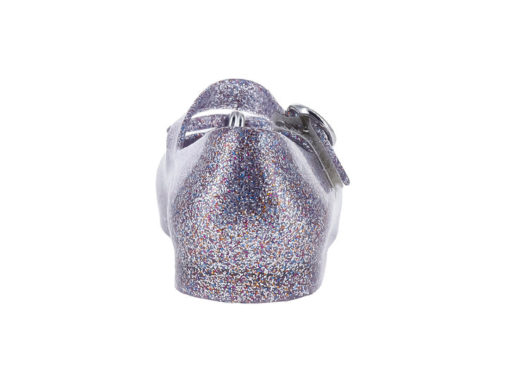 Zapato infantil color plata con acabado de glitter brillante y cierre de hebilla.