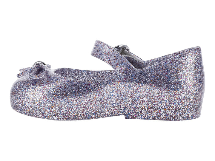 Zapato infantil color plata con acabado de glitter brillante y cierre de hebilla.
