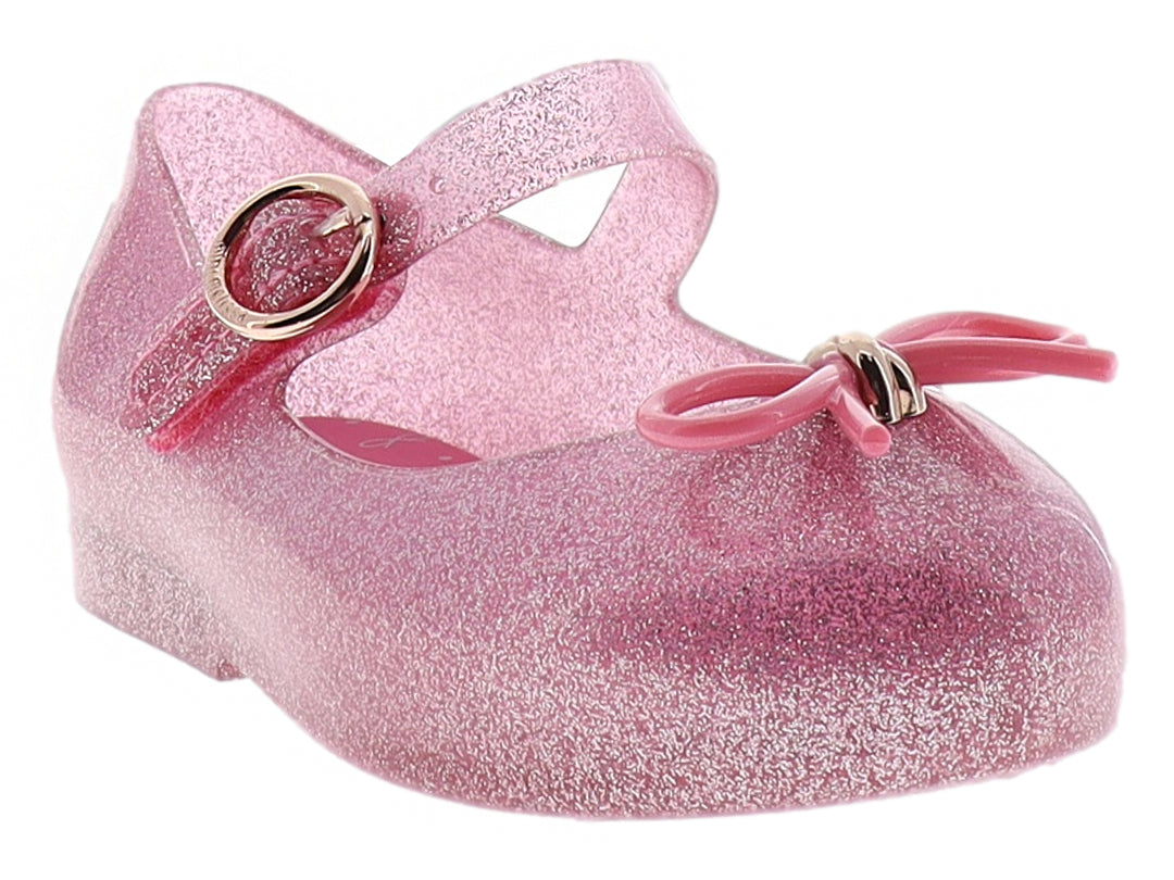 Zapato infantil Mini Melissa color rosa con glitter, moño decorativo y correa con hebilla dorada.