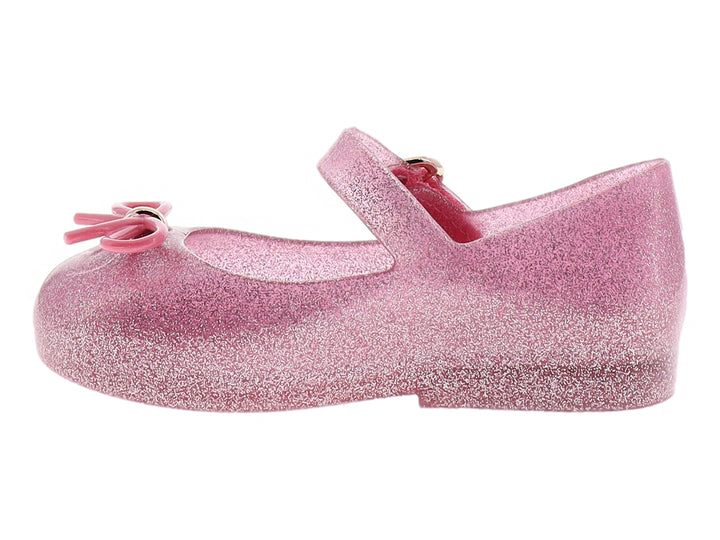 Zapato infantil Mini Melissa color rosa con glitter, moño decorativo y correa con hebilla dorada.