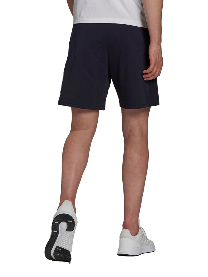 Hombre vistiendo pantalones cortos deportivos Adidas en color azul marino con logo blanco lateral.