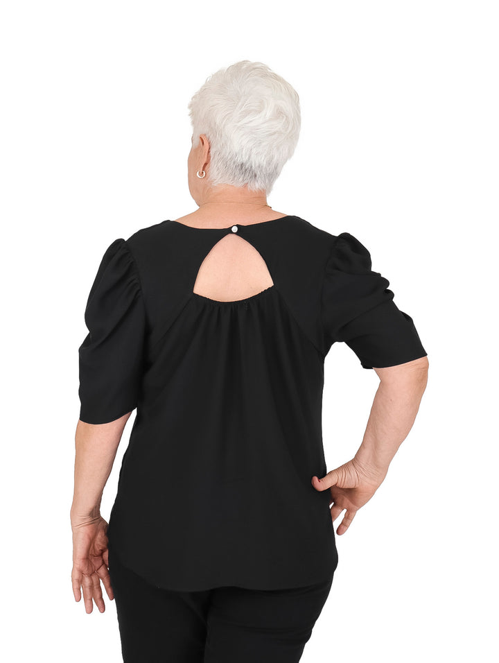 Mujer vistiendo una blusa color negro de manga corta con detalle abullonado en los hombros y cuello redondo.