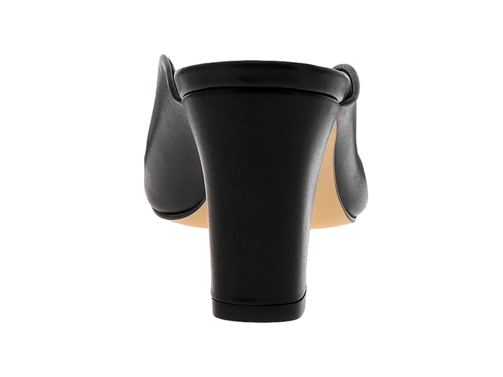 Zapato mule de piel negra con tacón grueso, punta afilada y un adorno metálico dorado en la parte frontal.
