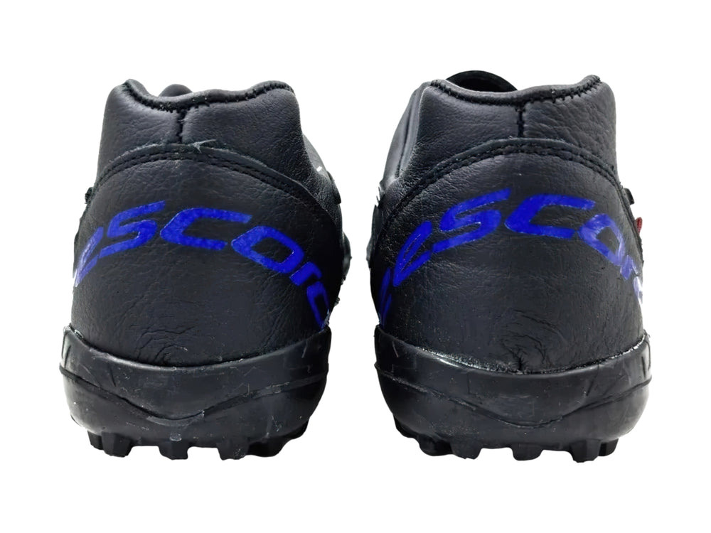 Zapato de fútbol turf color negro con detalles en azul rey y suela de goma con tacos pequeños.