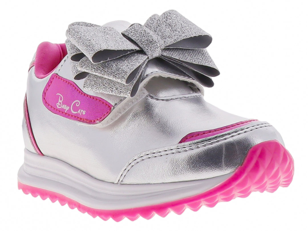 Tenis infantiles color plata con detalles en rosa y un moño brillante decorativo en la parte superior.
