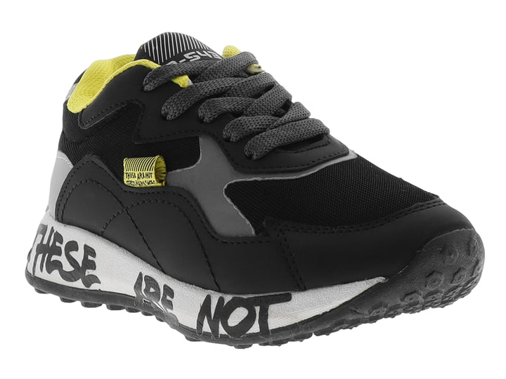 Tenis deportivos infantiles color negro con detalles en gris y amarillo, suela blanca con texto decorativo.