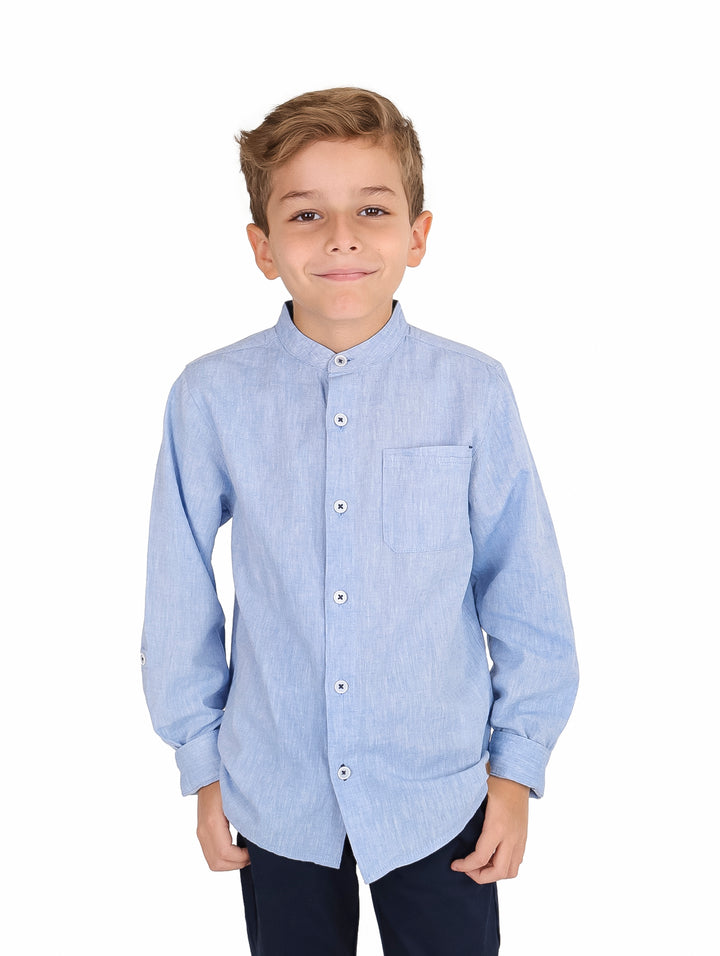 Niño vistiendo camisa de manga larga color azul claro con cuello mao y bolsillo frontal.