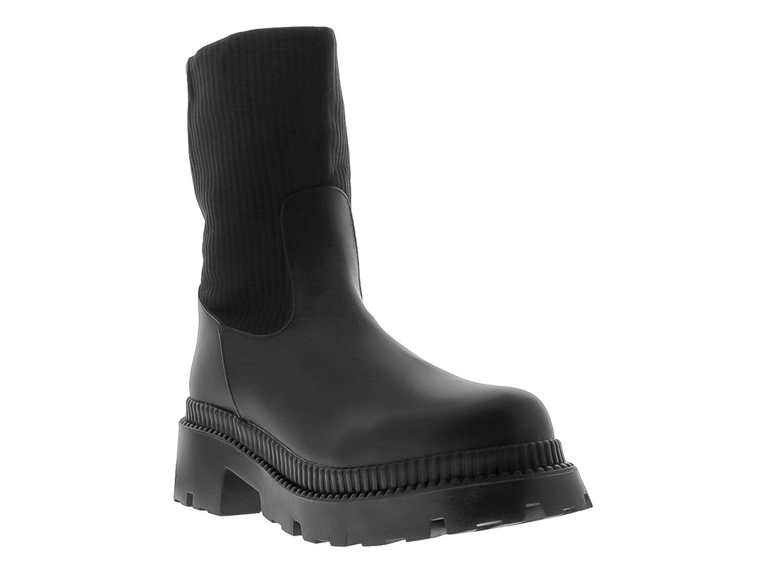Bota negra de caña elástica y suela track gruesa sobre fondo blanco.