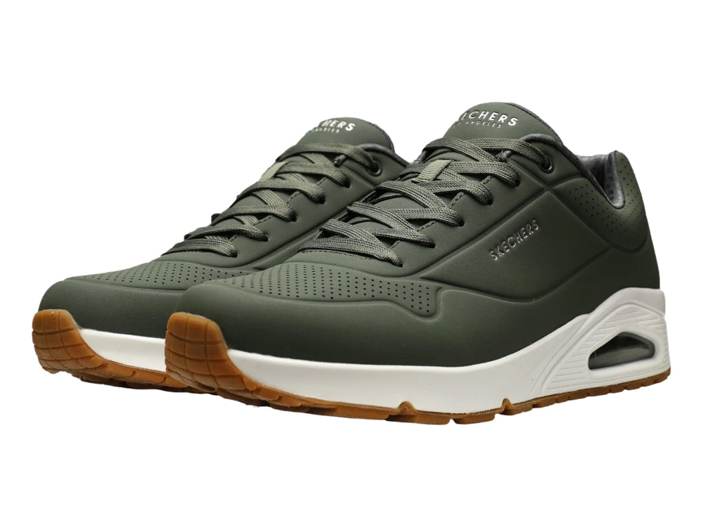 Tenis Skechers color verde oliva con suela blanca y amortiguación visible en el talón.