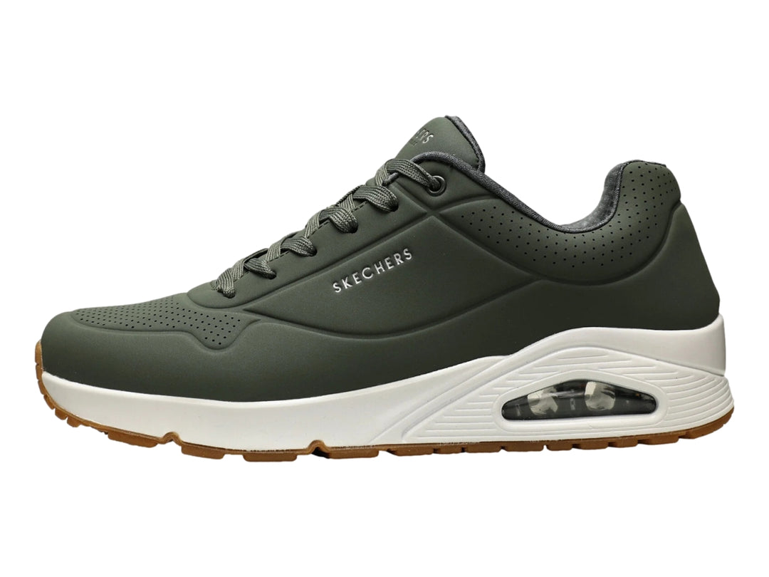 Tenis Skechers color verde oliva con suela blanca y amortiguación visible en el talón.
