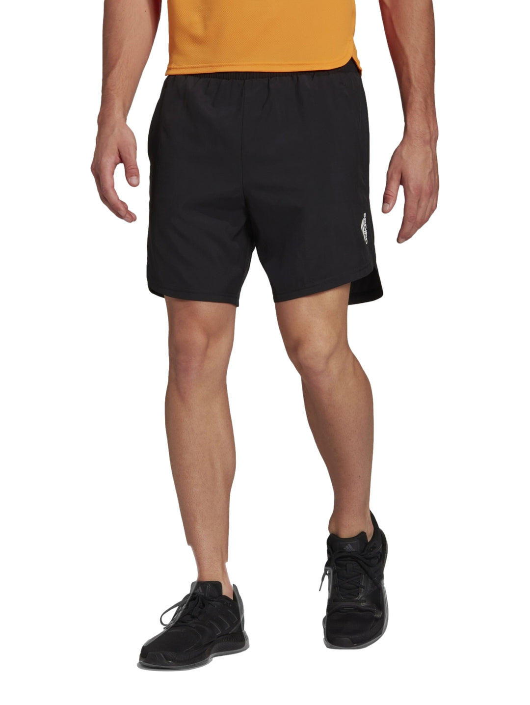 Hombre vistiendo pantalones cortos deportivos Adidas de color negro con camiseta naranja y tenis negros.