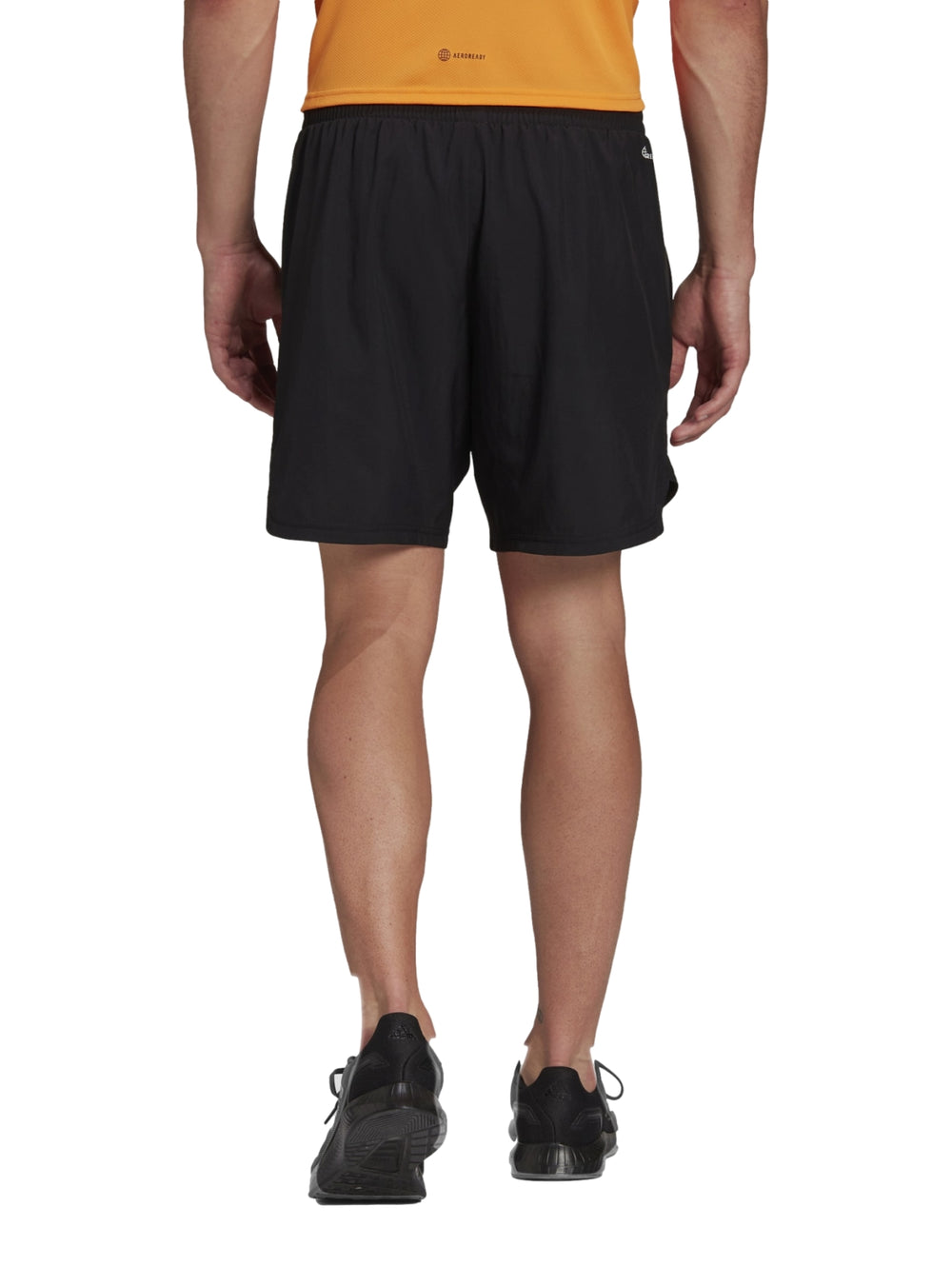 Hombre vistiendo pantalones cortos deportivos Adidas de color negro con camiseta naranja y tenis negros.