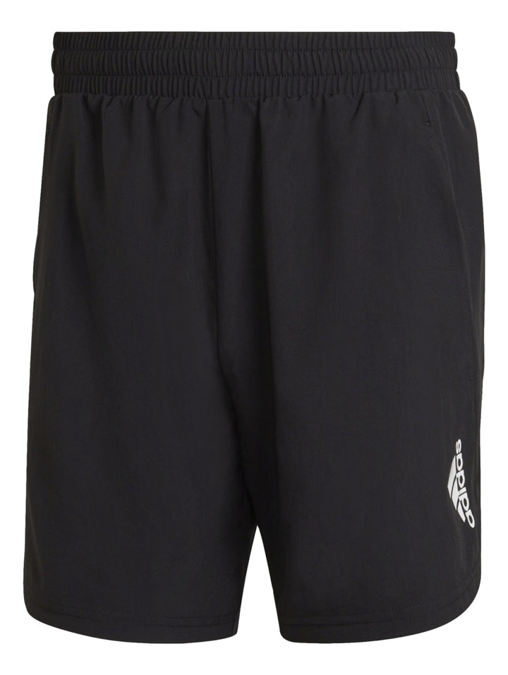 Hombre vistiendo pantalones cortos deportivos Adidas de color negro con camiseta naranja y tenis negros.