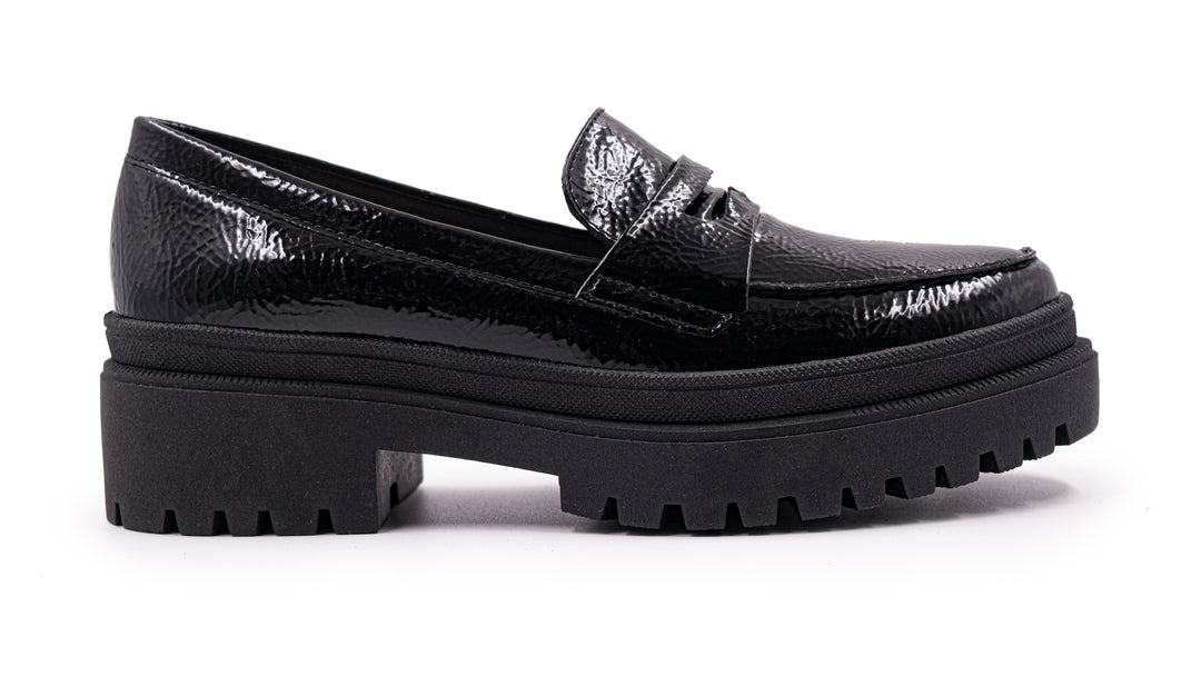 Zapato tipo mocasín negro de alto brillo con suela de plataforma gruesa y dentada.