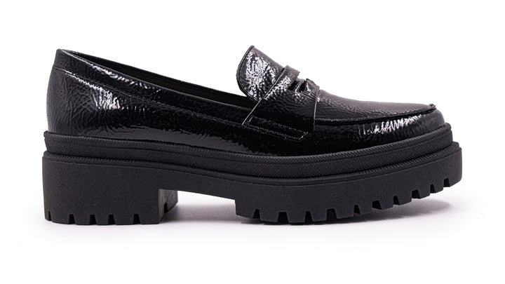 Zapato tipo mocasín negro de alto brillo con suela de plataforma gruesa y dentada.