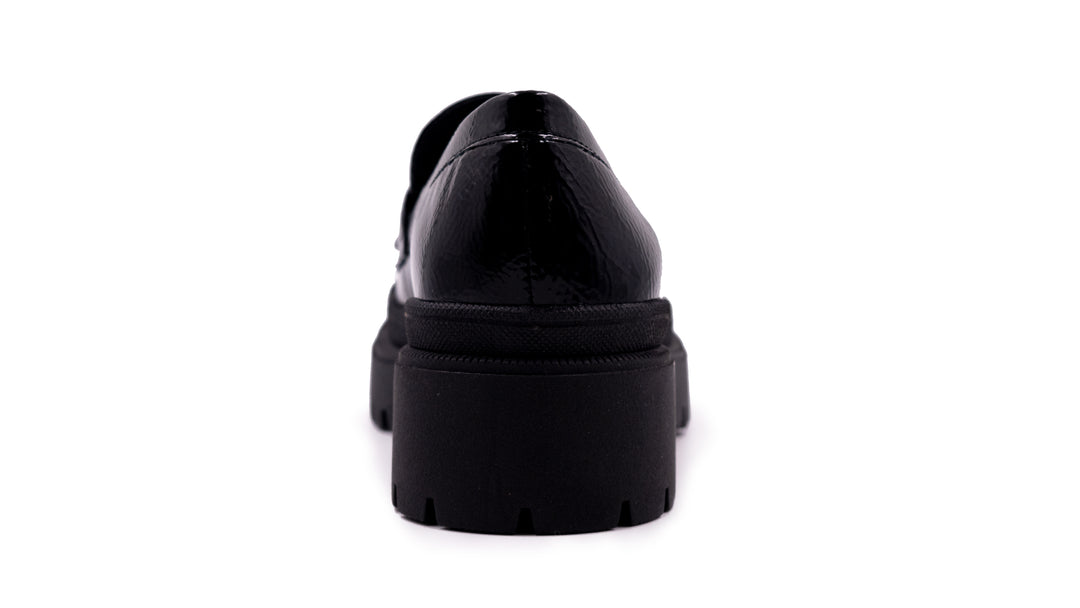 Zapato tipo mocasín negro de alto brillo con suela de plataforma gruesa y dentada.