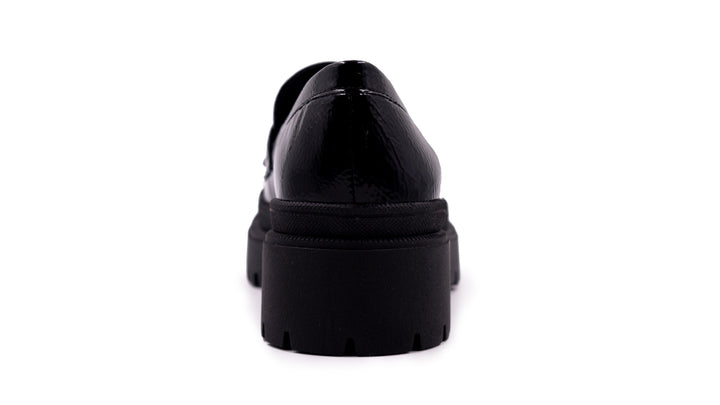 Zapato tipo mocasín negro de alto brillo con suela de plataforma gruesa y dentada.