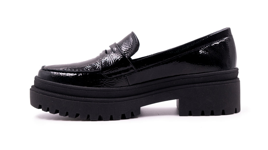 Zapato tipo mocasín negro de alto brillo con suela de plataforma gruesa y dentada.