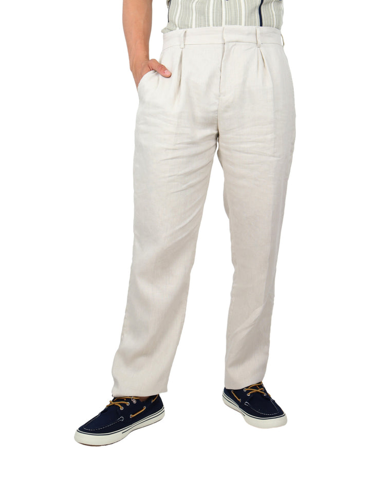 Hombre vistiendo pantalón color beige con pinzas y calzado azul marino sobre fondo blanco.