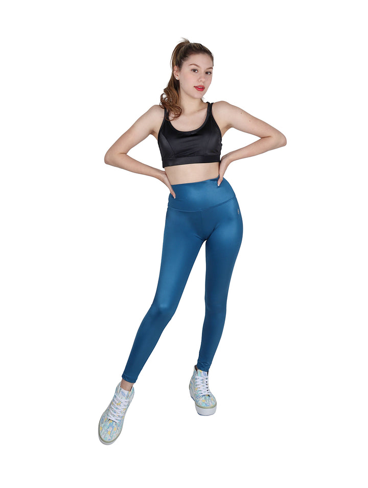 Mujer vistiendo leggings deportivos de color petroleo con talle alto y acabado brillante.