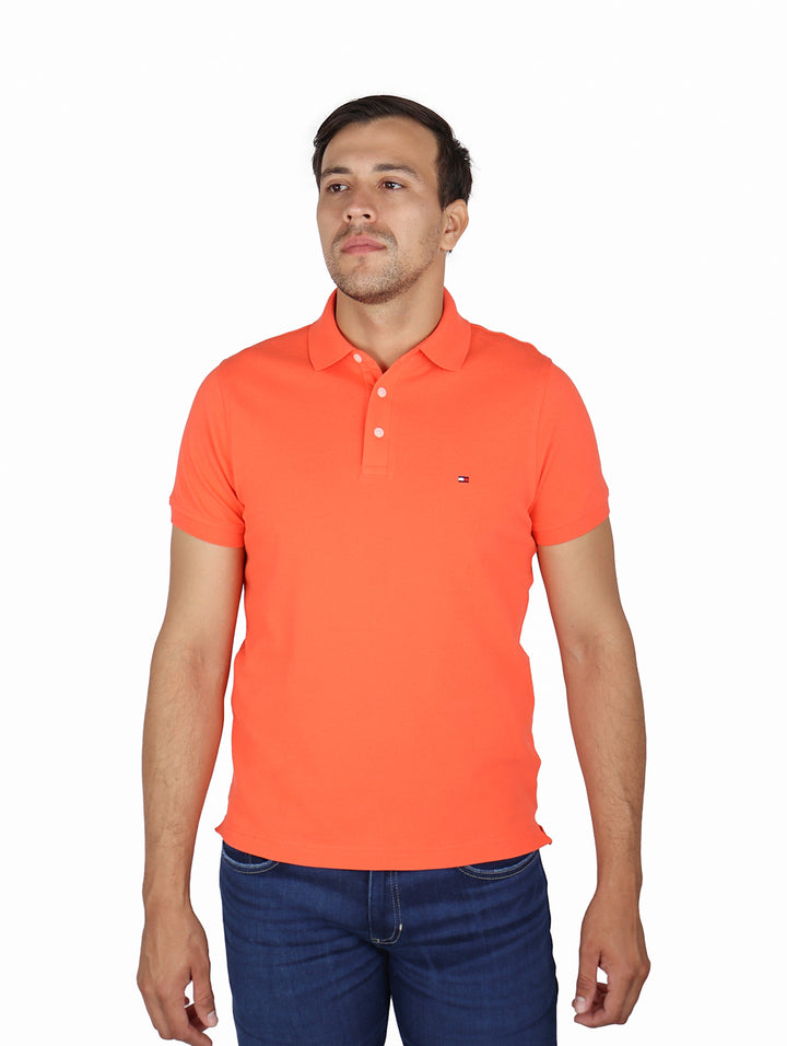 Hombre vistiendo una camiseta polo de color coral marca Tommy Hilfiger con ajuste slim y pantalones azules.