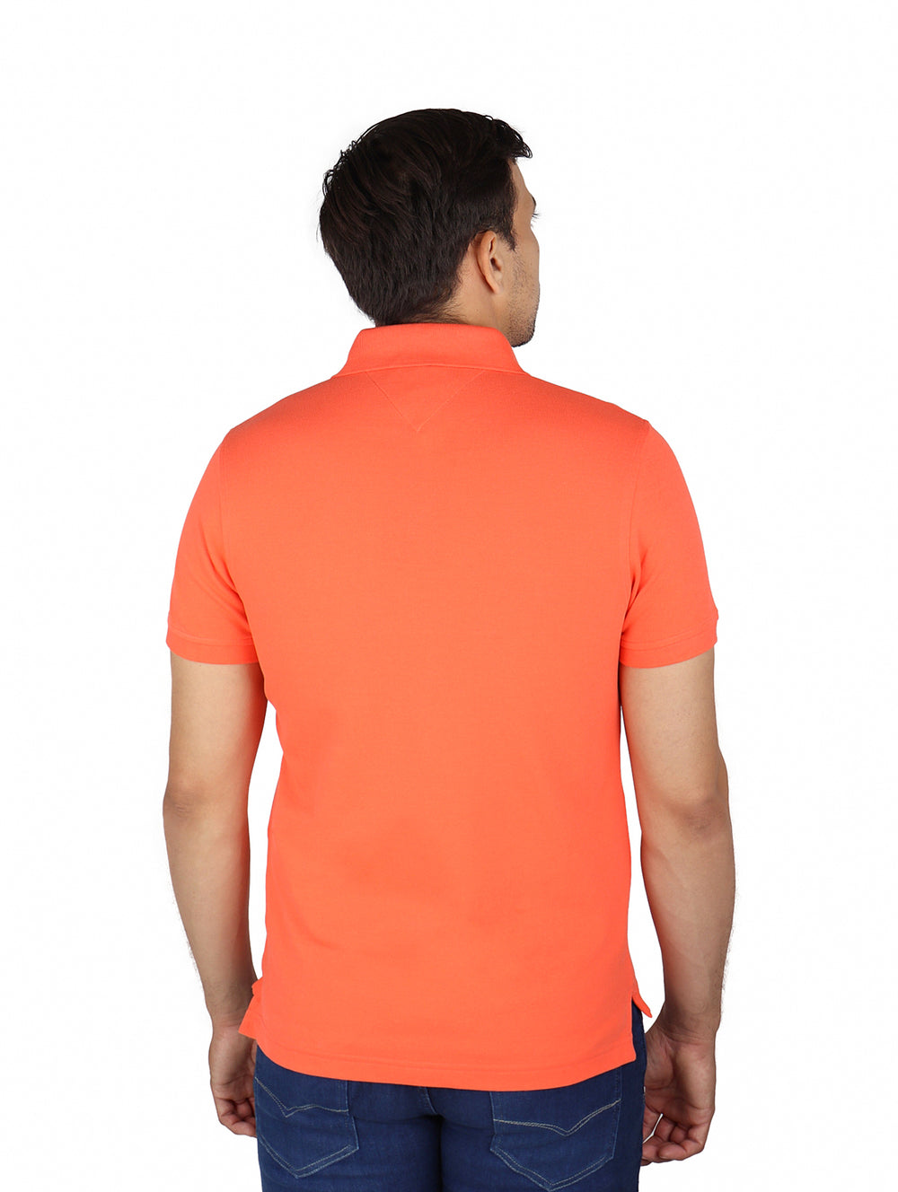 Hombre vistiendo una camiseta polo de color coral marca Tommy Hilfiger con ajuste slim y pantalones azules.
