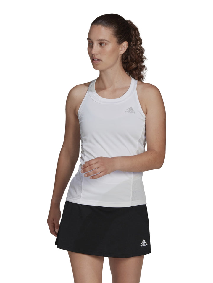 Mujer con camiseta deportiva blanca sin mangas Adidas y falda negra.