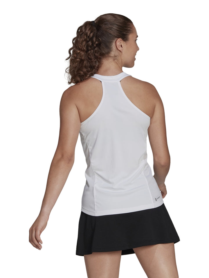 Mujer con camiseta deportiva blanca sin mangas Adidas y falda negra.