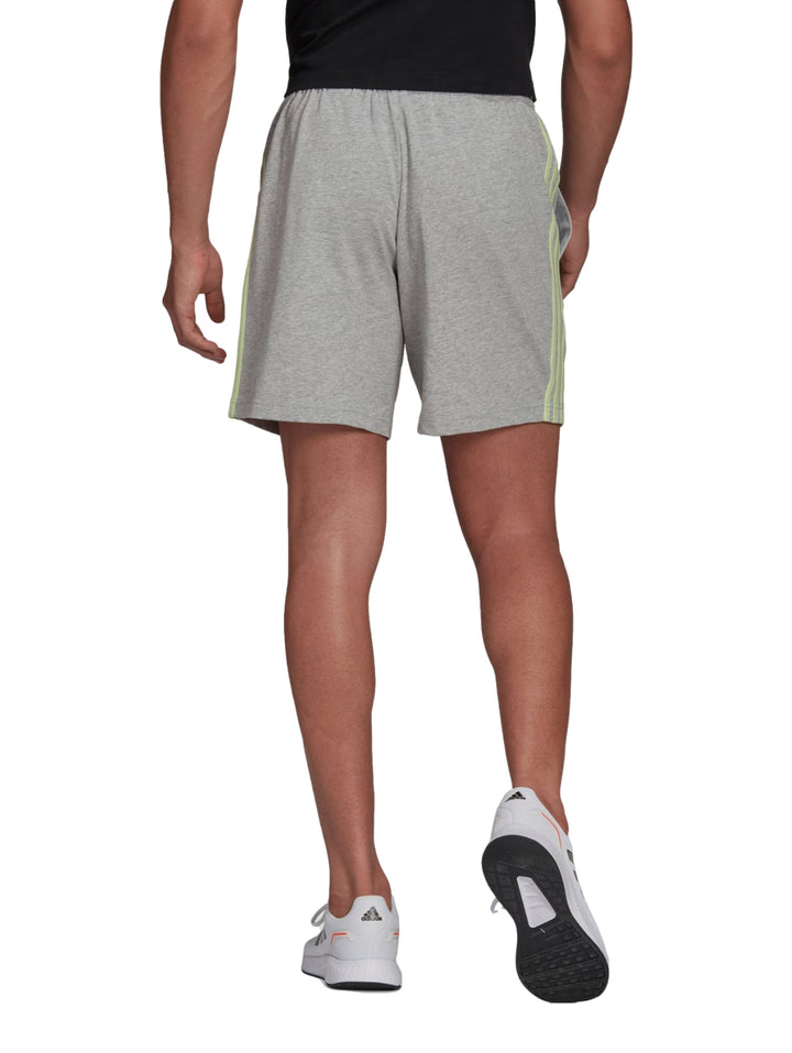 Hombre vistiendo pantalones cortos deportivos Adidas color gris con rayas laterales verde lima.